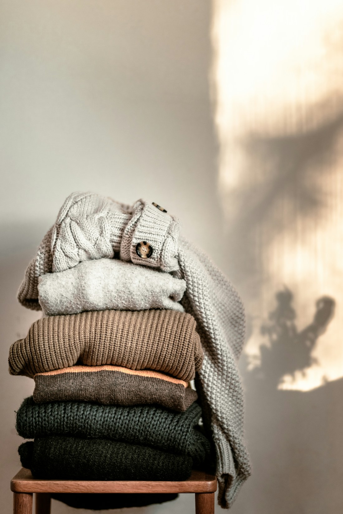 A stack of folded knitted throws in oatmeal, camel and soft grey